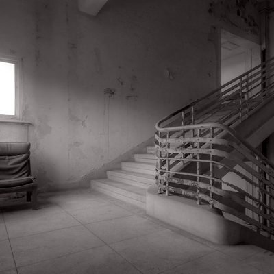 Abandoned building creepy dark moody staircase in dilapidated run down old deserted hospital school ruin with a single empty chair indoors on stairs landing no one there